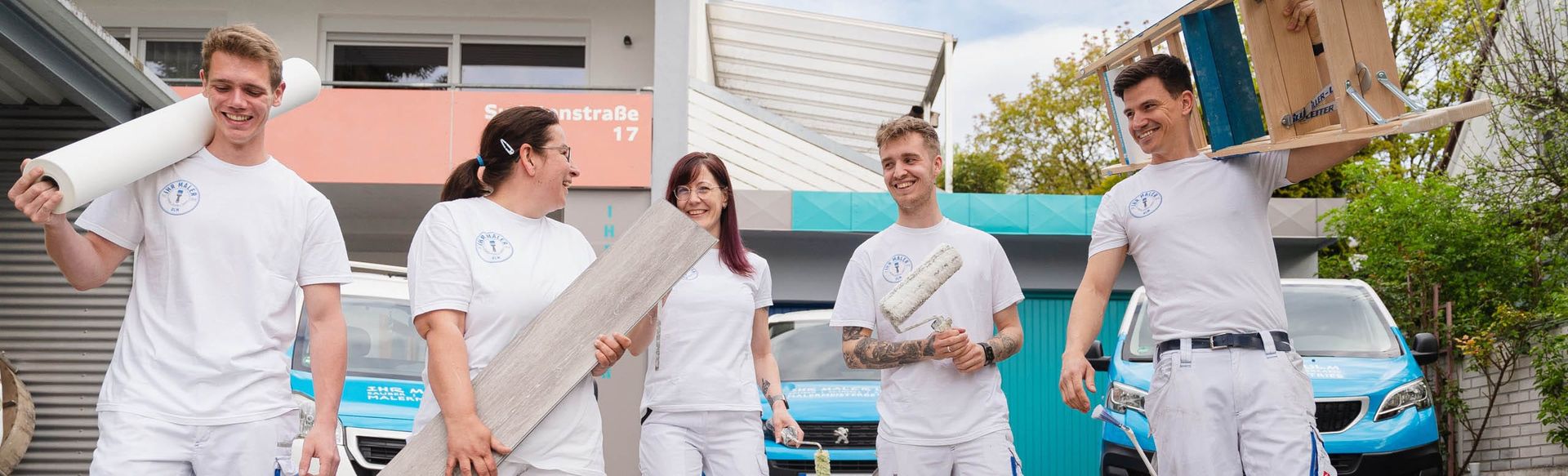 Fünf Handwerker mit Werkzeugen vor einem Gebäude.